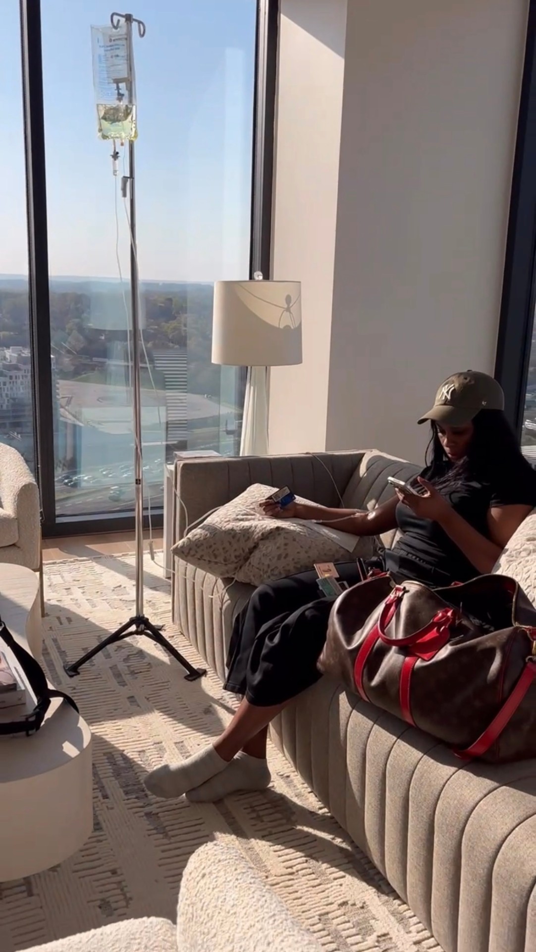 IVybe client receiving an IV drip on a sunlit couch in a high-rise apartment overlooking Atlanta